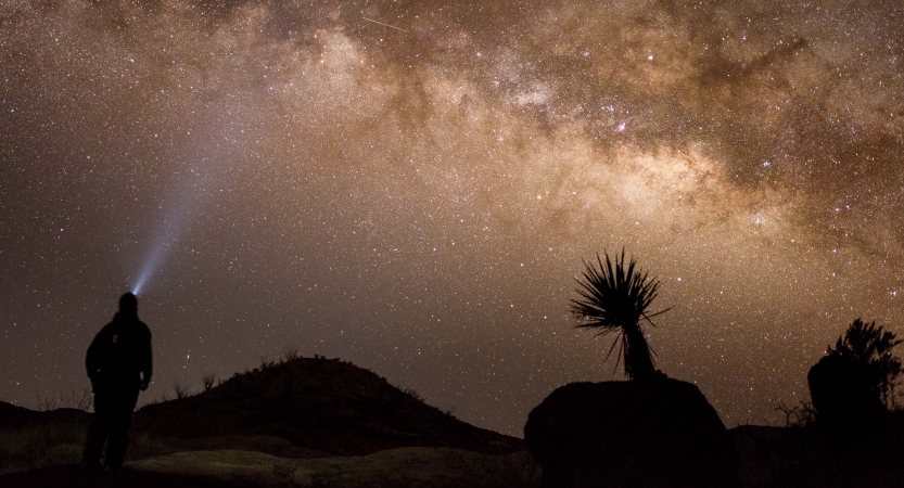 a person wearing a headlamp looks up at a brilliantly lit night sky